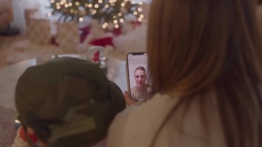 Mother and child sitting at home during christmas talk to the father via a video call on a smartphone