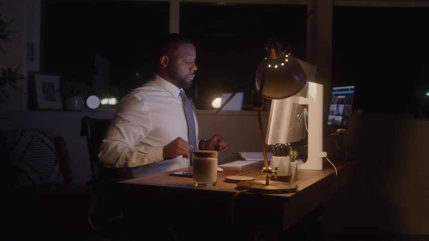 A tired man working in his office at night putting his hands on his head in exhaustion then returning to type on his computer keyboard