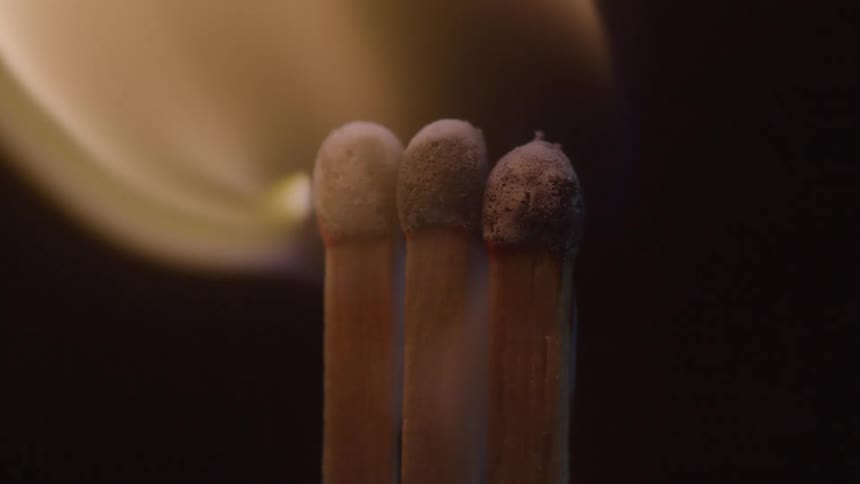 Three matchsticks stand close together as a flame ignites them from the left side the flame slowly dies out