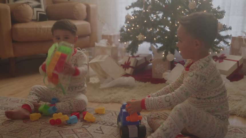 Two male children play with toys while sitting on the floor in a living room during daytime