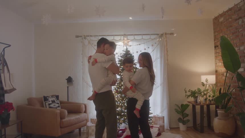 A couple stands in front of a christmas tree with their two children with the father holding one child and the mother holding the other