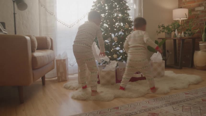 Children in christmas pajamas run towards the decorated christmas tree