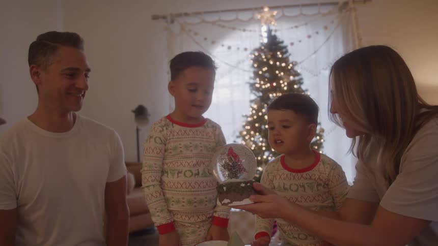 Family gathered around a snow globe in front of a lit christmas tree