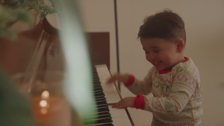 A young boy in festive pajamas joyfully plays the piano