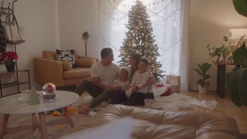 A family sits together by a decorated christmas tree in their living room
