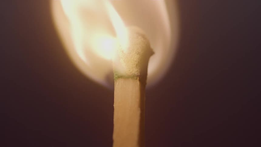 A matchstick is engulfed in flames in a dark room