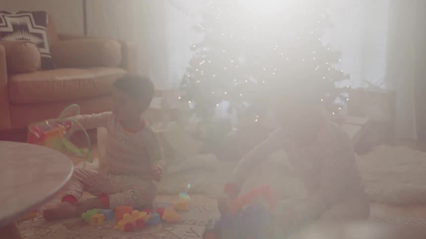 Two children in pajamas playing with toys on the floor in front of a christmas tree