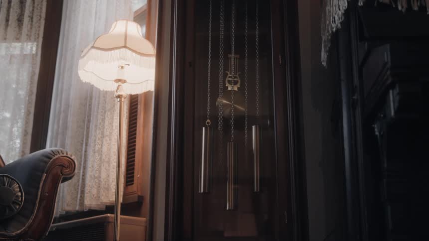 The interior dcor of a living room features a lit lamp and a grandfather clock on the wall its pendulum swinging left and right