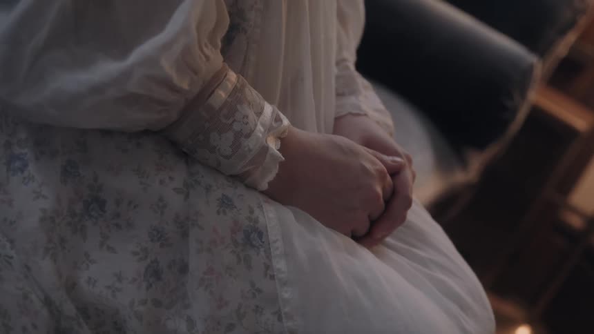 Clasped hands rest on a light dress with lace sleeves