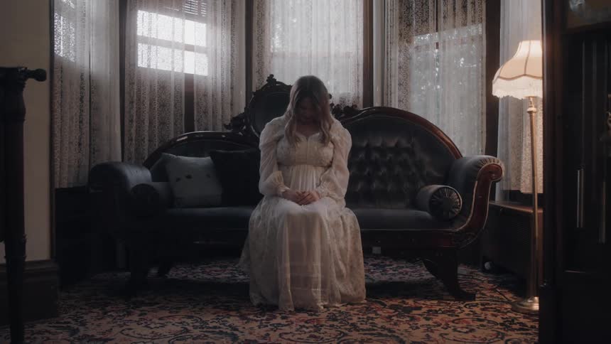 A woman sits on the couch wearing a white dress