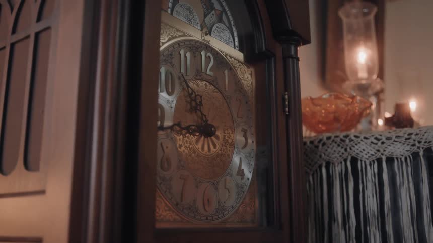 A grandfather clock stands beside a table with a candle burning inside a glass
