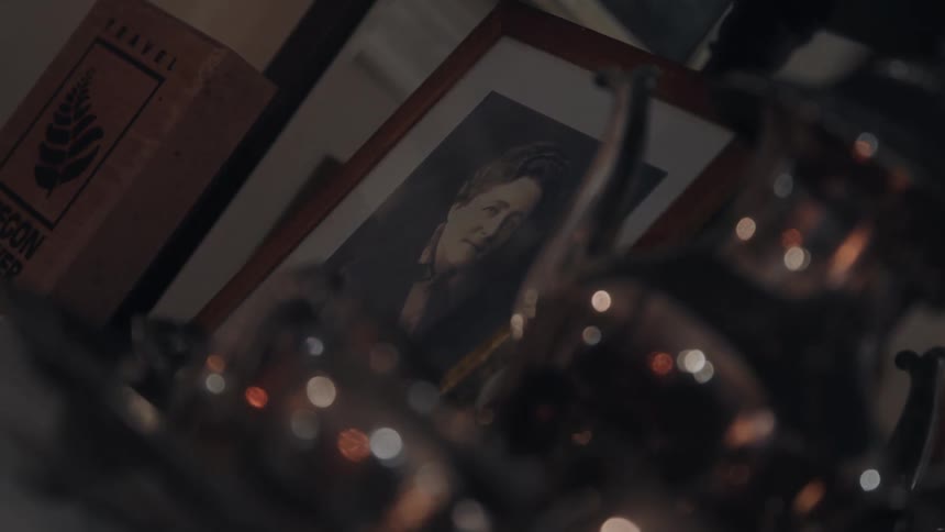 A low light close view shows a framed black and white portrait of a woman sitting on a surface next to a box and behind several blurred reflective objects