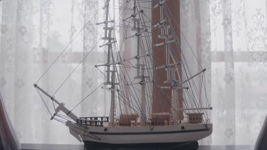 A replica of a historical vessel sits on a surface beside a window indoors at midday