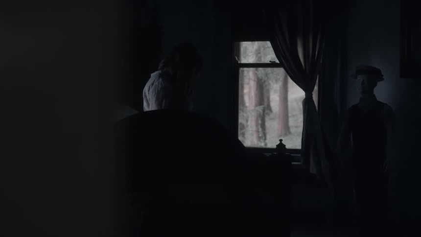 Person standing in a dark bedroom next to a window lit by outside light