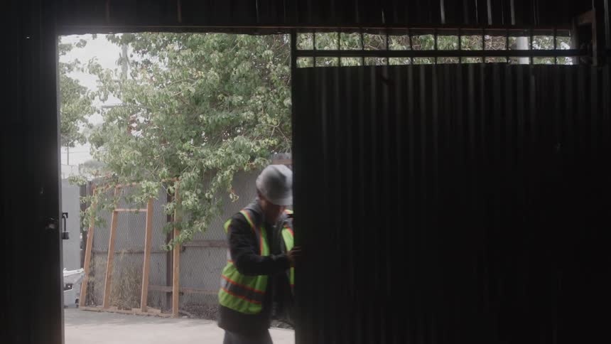 Worker wearing a safety vest and helmet opens a metal gate