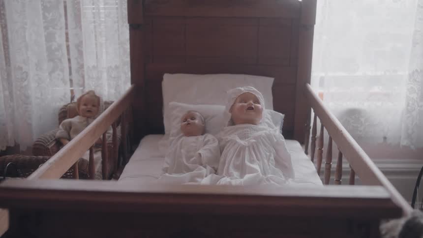 Antique wooden crib with dolls dressed in white lying down