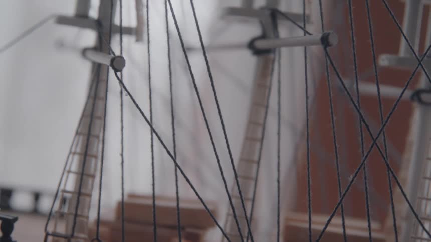 A close view of a large intricate model ship shows the rigging and masts with a blurry background