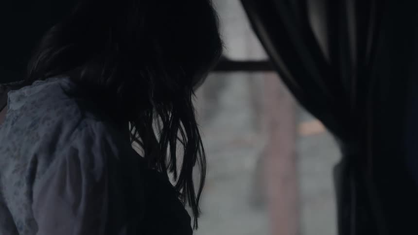 The woman looks out the window from inside a dark room