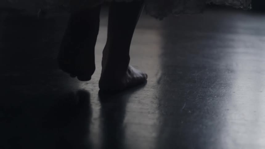A persons bare feet glide across a dark floor