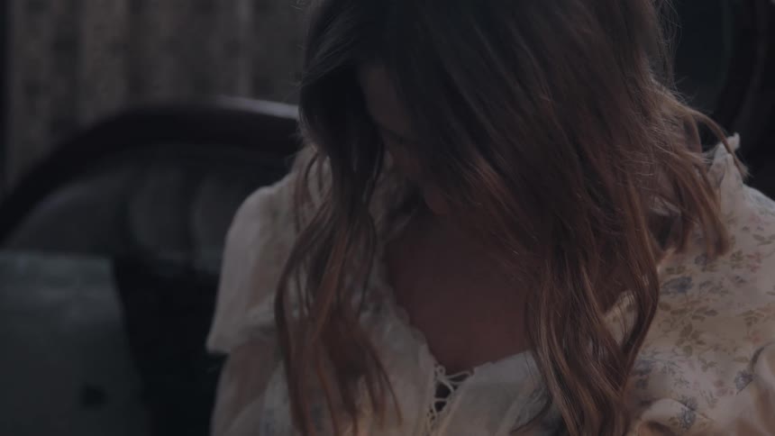 A close view shows a woman with long dark hair wearing a white and brown floral shirt with their head down and hair covering their face