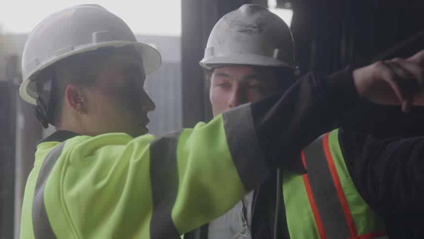 Construction workers wear helmets and reflective vests while having a conversation