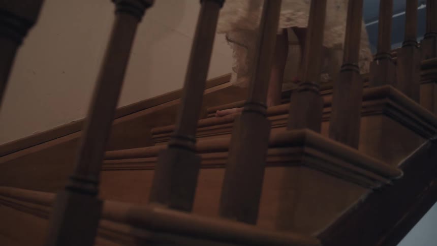 Person walks up wooden stairs barefoot wearing a light dress