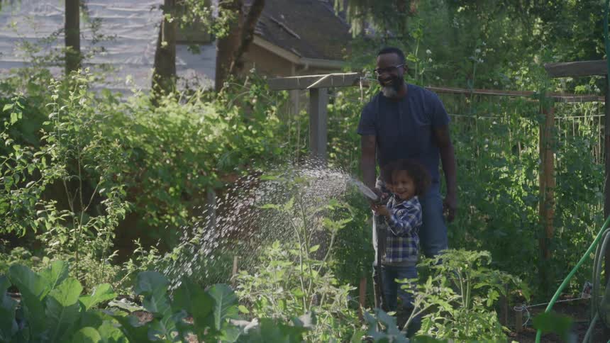 Man and child water the garden together using a hose