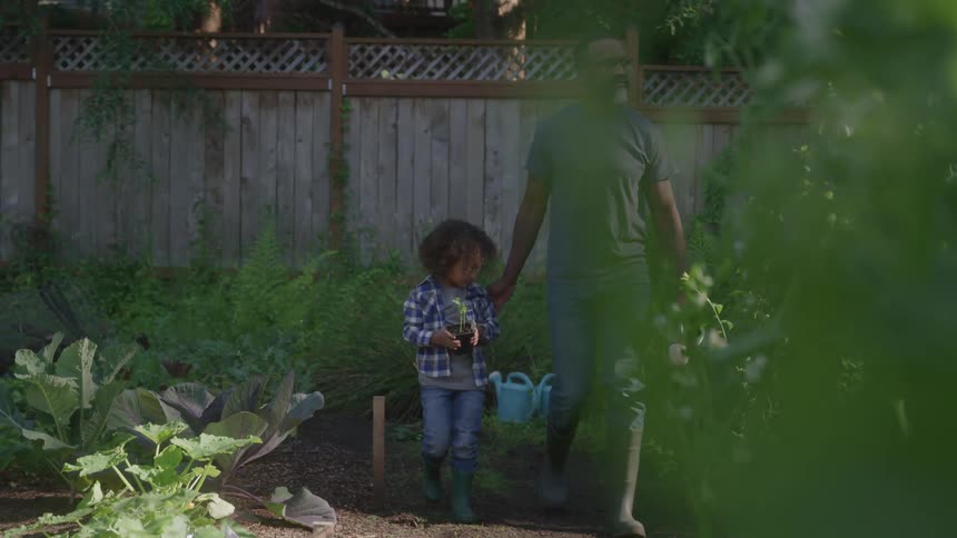 A man and child walk together in a garden holding hands