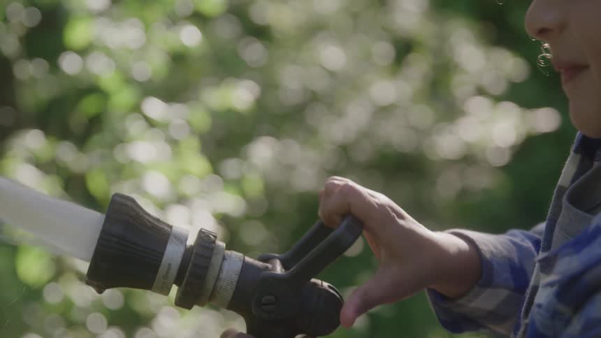 Child holding a hose with water spraying wearing a blue plaid shirt