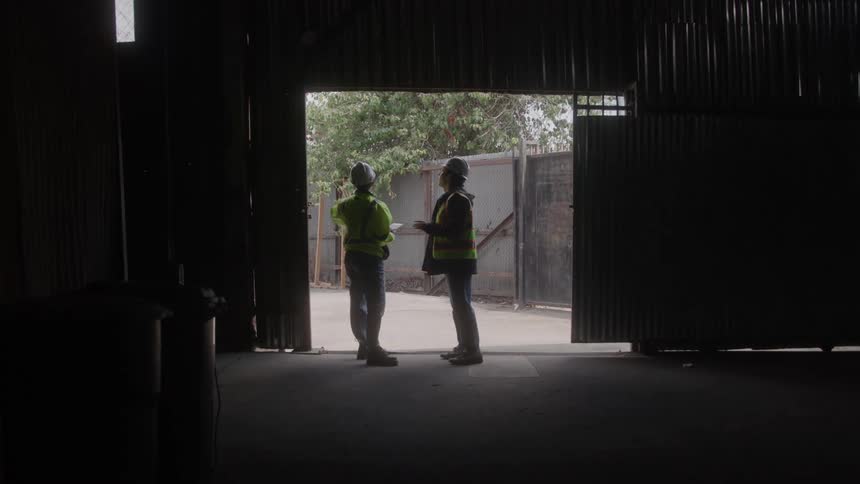 Two construction workers in full protection gear talking while standing at a garages door