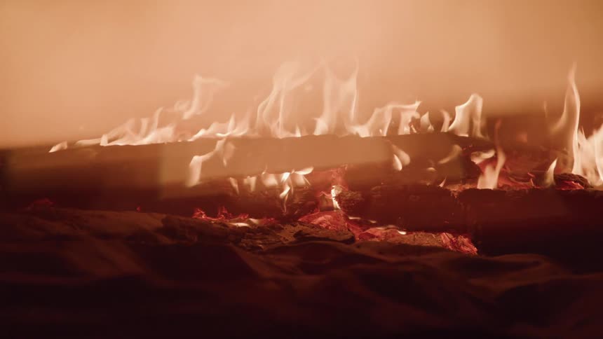 Close up of wooden logs in flames on the sand outdoors at night