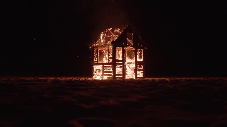 Small wooden houselike structure burning in flames at night