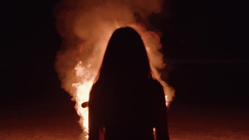 Silhouette of a person watching a large bonfire burning