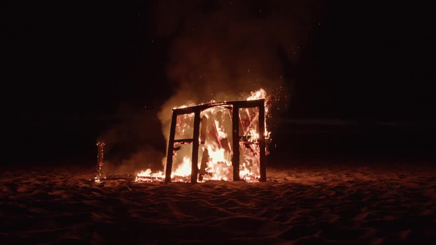 A small wooden building up in flames outdoors at night