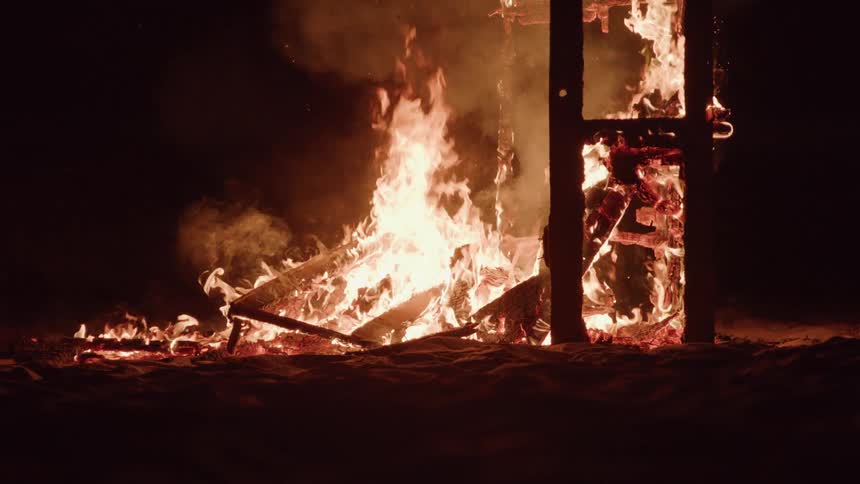 Flames glow and smoke rises in a burning building in the darkness