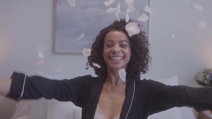 Smiling woman with open arms is surrounded by white petals in the air