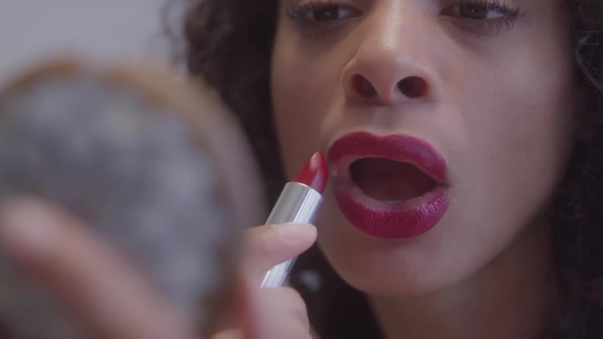 Woman applying red lipstick in front of a handheld mirror