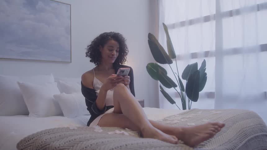 A woman sits on the coach and texts on her phone