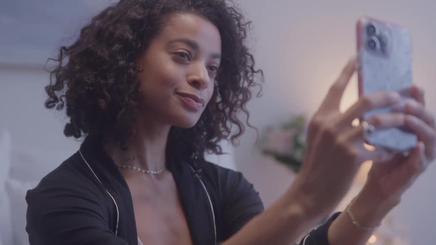 Close up of a young black woman taking selfies with a mobile phone in a bedroom during daytime