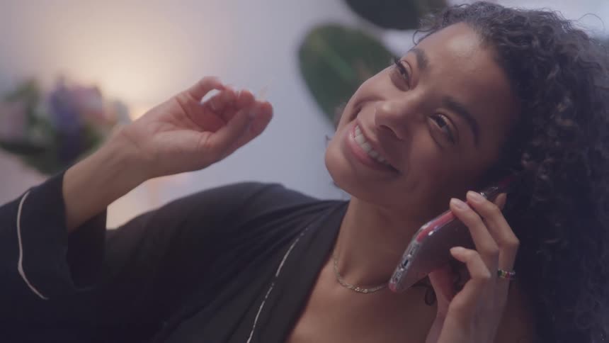 A woman smiles while talking on the phone in a cozy bedroom