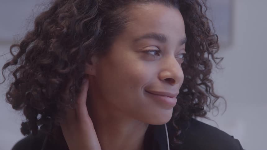 A person with curly hair is looking into the camera they smile and then turn their head to the side