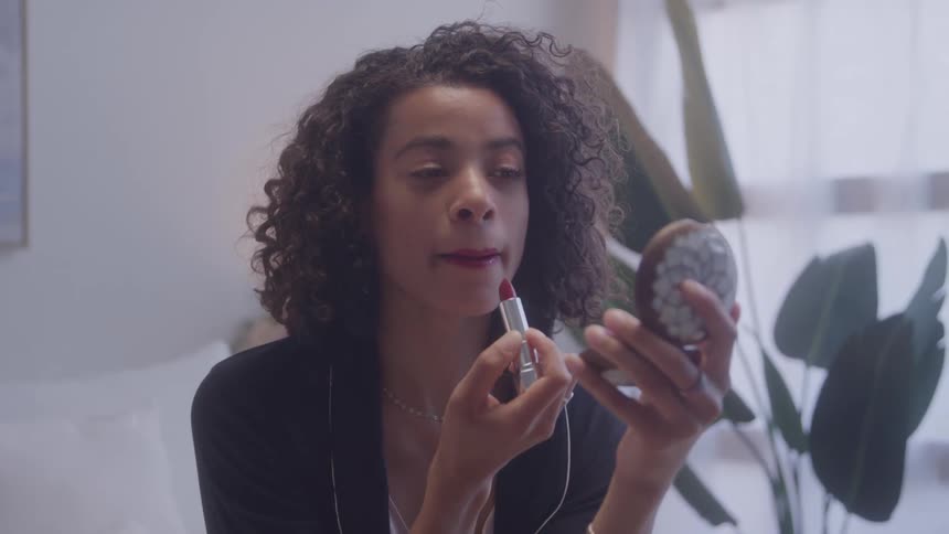 Woman applying lipstick and looking at mirror indoors
