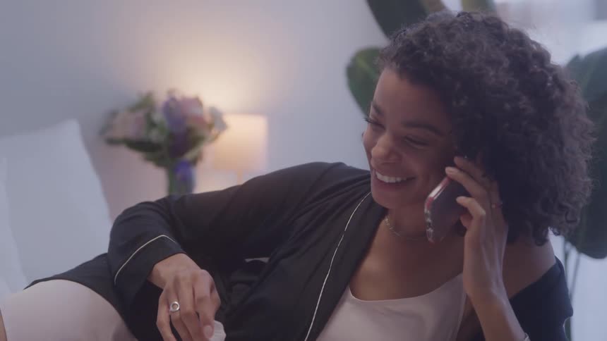 A smiling woman talks on the phone in bedroom
