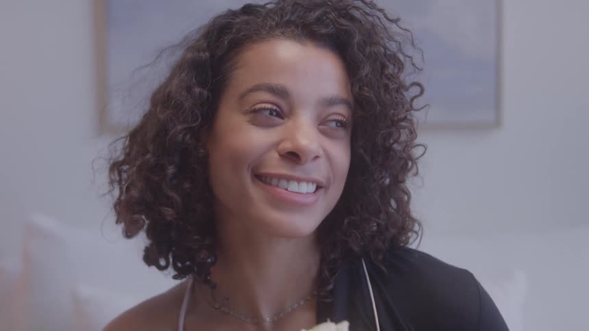 A young woman smiles as she smells a flower shes holding