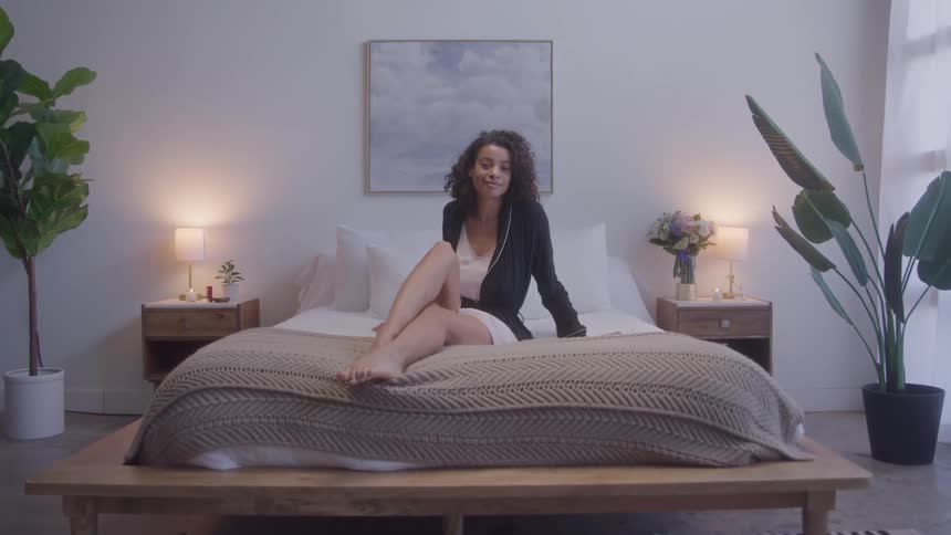 A young black woman sitting in the middle of a bed in a bedroom during daytime