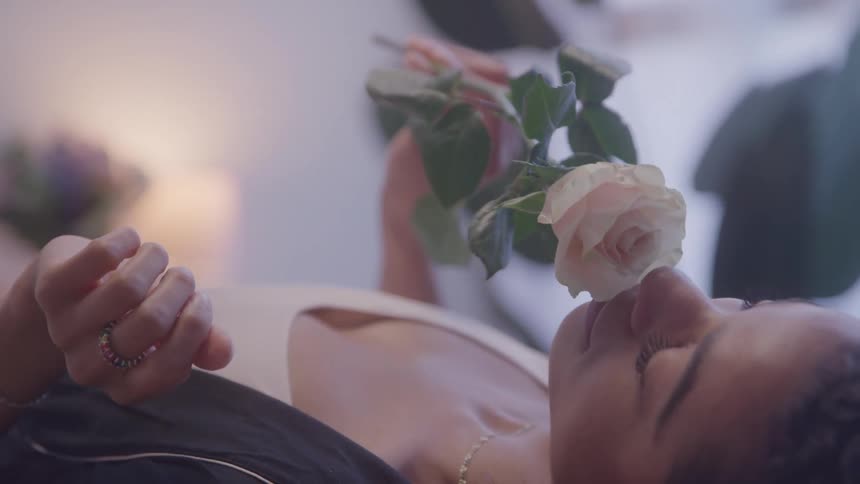 Woman lying down observing a lightcolored rose in her hand