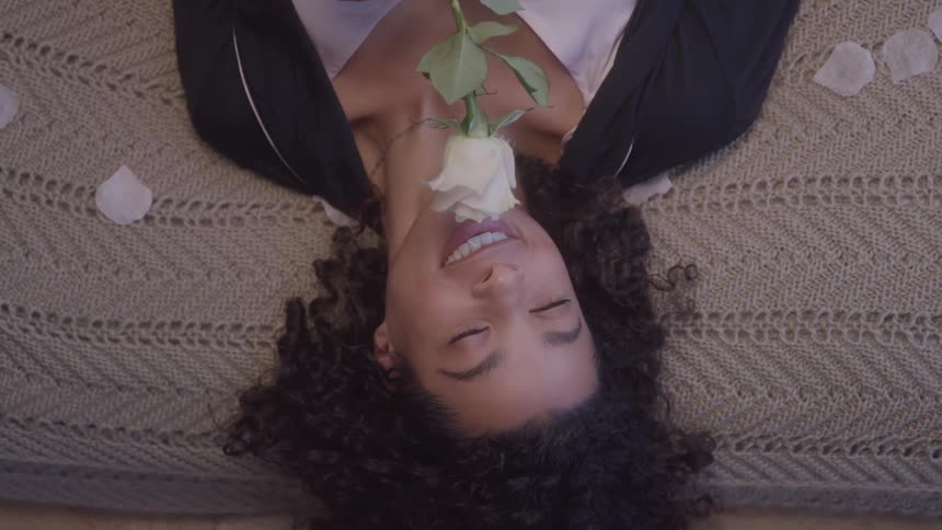 Girl with a rose in her hand smiling and throwing herself onto the bed
