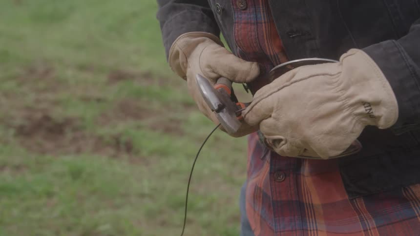 A persons hands in leather gloves using a wirecutter to cut a fence wire
