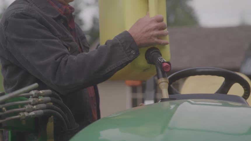 A man is pouring fuel from a yellow container into a tractor