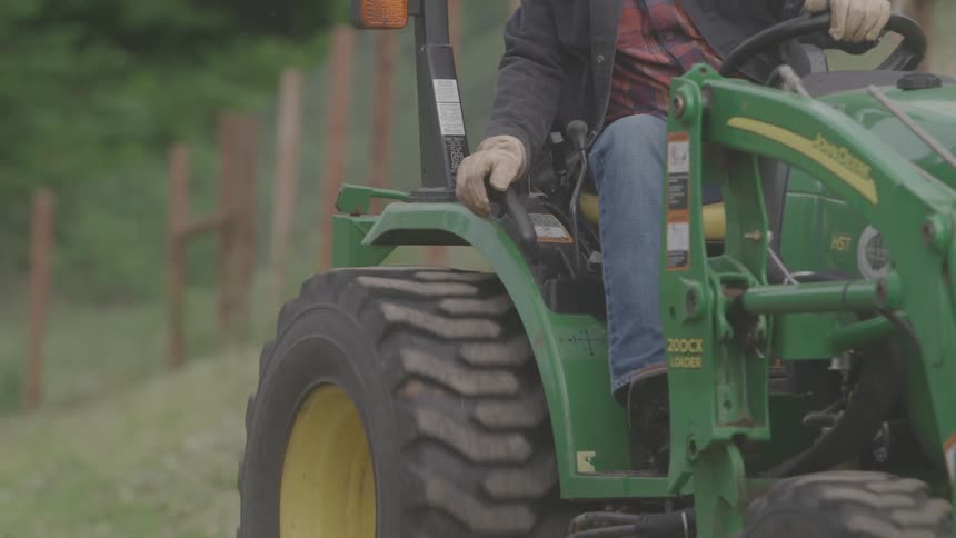 A man reverses a tractor on a farm at midday